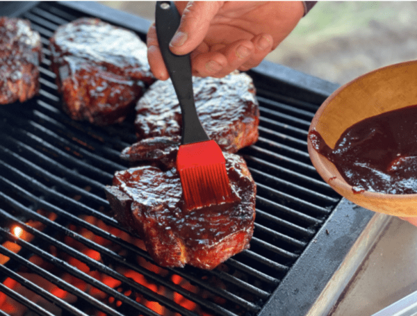 Grilling steaks with BBQ sauce and a brush.